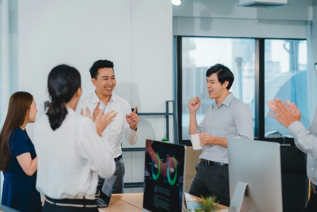 Asian Traders in an office celebrating and holding up fingers to calculate their winnings