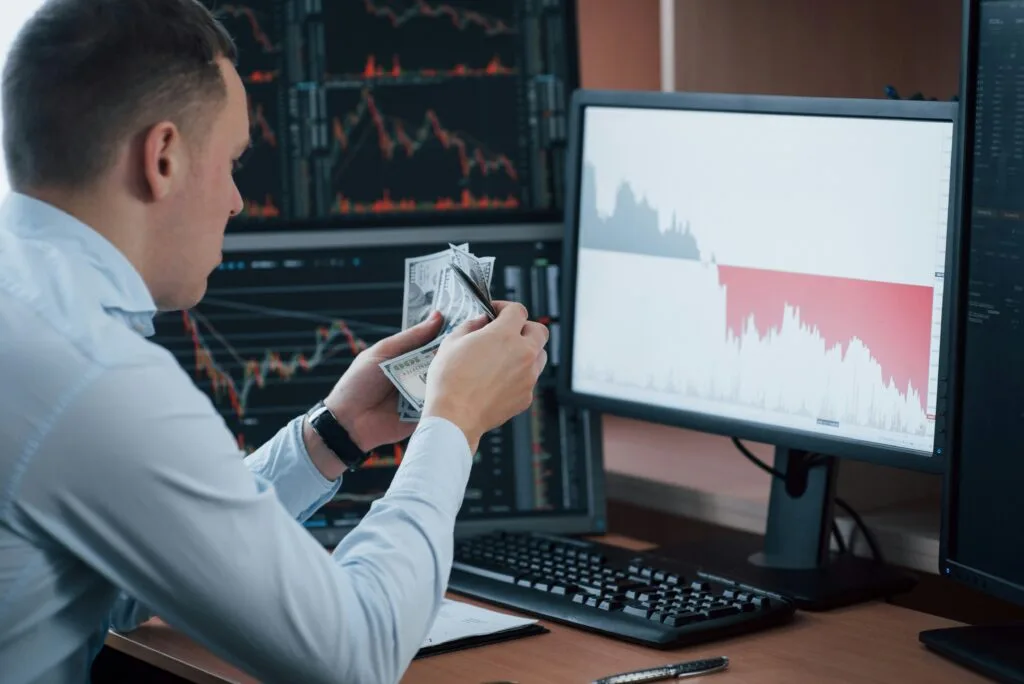 Man looking at trading screen with USD in his hand