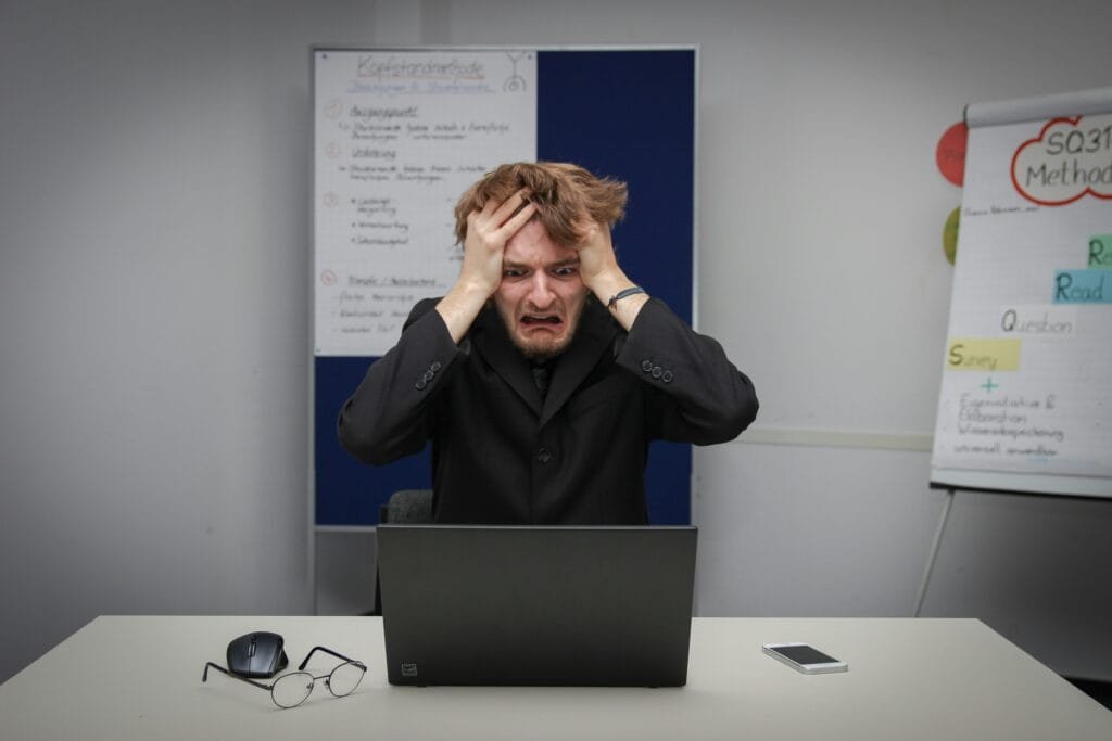 Man with head in hands looking at computer screen panicking 